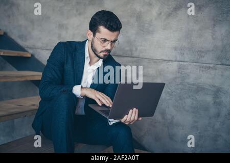 Portrait of his he nice attractive focused concentrated bearded guy financier holding in hands laptop browsing reading finance information sitting on Stock Photo
