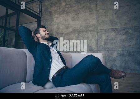 Profile side view portrait of his he nice good-looking imposing attractive luxurious cheerful cheery bearded guy wearing jacket sitting on cozy divan Stock Photo
