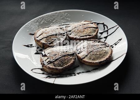 homemade chocolate pancakes served on a white plate over black texture background. Beautiful pancakes. Stock Photo