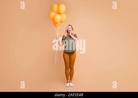 Full body photo of amazing charming blond lady emotional surprise holding bright orange balloons came birthday party wear green t-shirt trousers Stock Photo