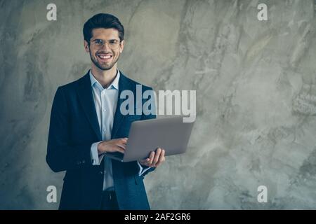 Photo of cheerful positive toothy beaming man holding laptop with hands smiling toothily cheerfully near empty space browsing isolated grey color Stock Photo