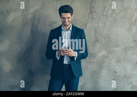 Portrait of positive cheerful ceo worker using smartphone send sms to colleagues having fun on his workplace wearing stylish pants isolated over grey Stock Photo