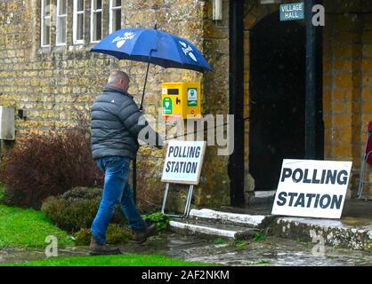 Walditch, Dorset, UK.  12th December 2019. A man with an umbrella arriving in the rain to vote at the Polling Station at Walditch in Dorset on a wet General Election day.  Picture Credit: Graham Hunt/Alamy Live News Stock Photo