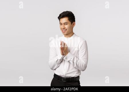 Hideous, sly handsome young asian male entrepreneur have something evil or genius in mind, rub palms near chest, squinting mysterious and smirk, have Stock Photo