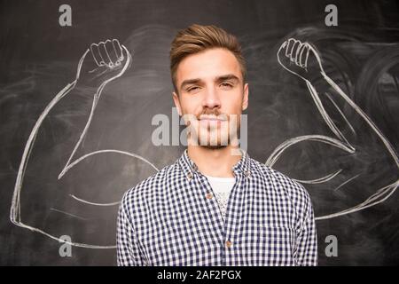 Young man against the background of depicted muscles on chalkboard. Stock Photo