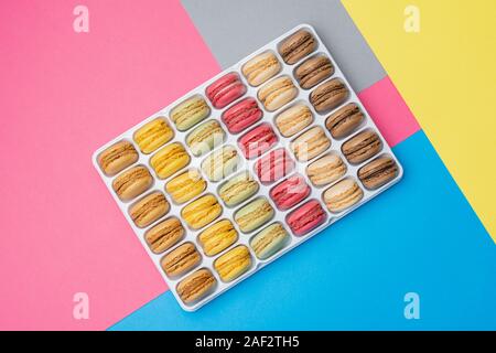 Classical french dessert. Colorful macarons on creative pink blue yellow grey background stacked in a box, selective focus Stock Photo