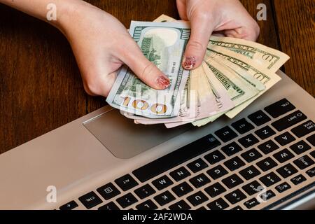 Different objects on wooden office desk. Modern wooden office desk table with laptop keyboard and hands holding dollars money. Stock Photo