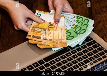 Different objects on wooden office desk. Modern wooden office desk table with laptop keyboard and hands holding euro money. Stock Photo