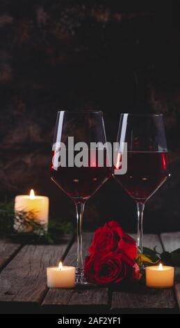 Two glasses of wine with red roses and burning candles on a rustic wooden table and background Stock Photo