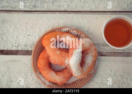 Russian fast food bagel pyshki and paper cup with tea or coffe on wooden table, covered with snow, winter snack in the park. Stock Photo
