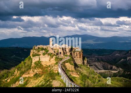 Civita di Bagnoregio, an old etruscan settlement, located on top of a volcanic tuff plateau, illuminated by the setting sun, dark thunderstorm clouds Stock Photo