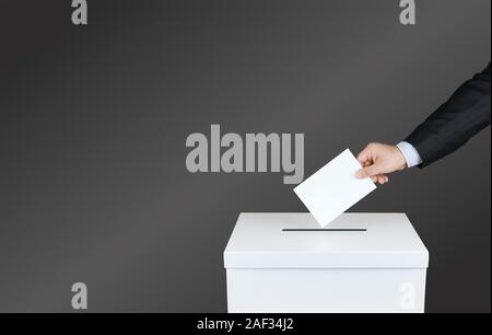 Hand of a person use a vote into the ballot box in elections. With black background Stock Photo