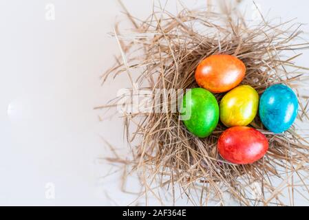 Multi-colored Easter eggs lie together in a straw on a white background. Copy space for design. View from above. Stock Photo