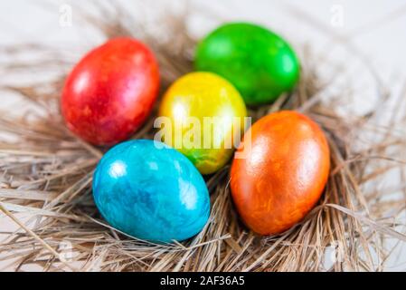 Multi-colored shiny Easter eggs lie together on a straw in the form of a nest on a white background. Close-up. View from above. Stock Photo