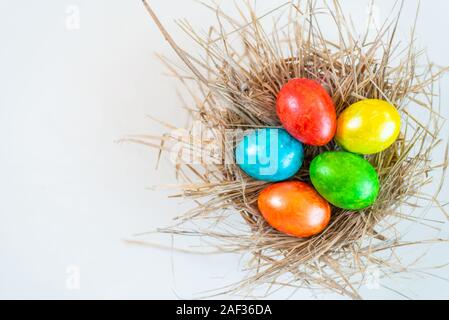 Multi-colored Easter eggs lie together in a straw on a white background. Copy space for design. View from above. Stock Photo