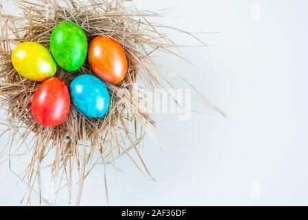 Multi-colored Easter eggs lie together in a straw on a white background. Copy space for design. View from above. Stock Photo