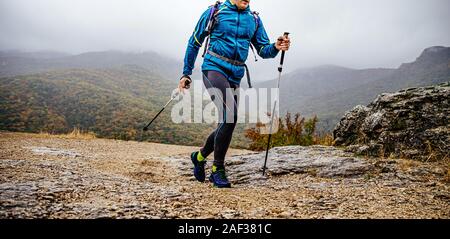 man with trekking poles walk mountain trail in rainy autumn weather Stock Photo