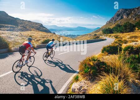 Road cycling photo. Two triathlete train in beautiful nature. Sea and mountains in background. Alcudia, Mallorca, Spain Stock Photo