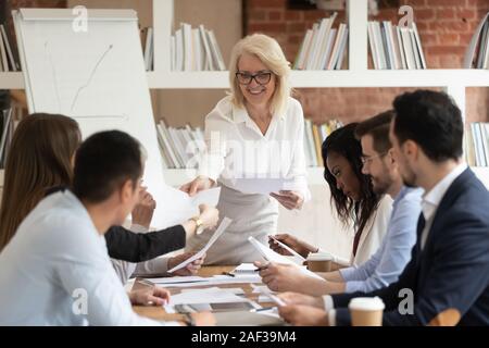 Middle-aged businesswoman boss giving financial report to diverse employees Stock Photo