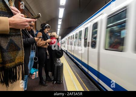 People stand on the platform at Tribunal Madrid Subway Station using their mobile phones as a train arrives into the platform. Stock Photo