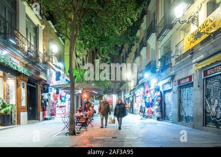 A view down a city Centre street called Calle de Postas in Madrid, Spain at night. Trees run down the middle of the street which is lit up by  lights. Stock Photo