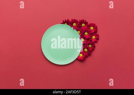 Spring table settings with green empty dish and red flowers ornament, on a red background. Eco-friendly empty platter. Minimal food background. Stock Photo