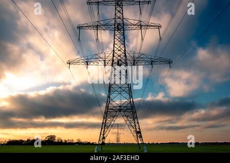 High voltage pylons in a beautiful landscape with colorful clouds in wintertime, taken in the Netherlands province Overijssel Stock Photo