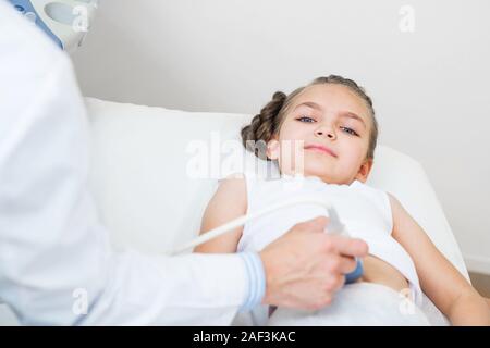 Sonographer moving transducer on belly of little girl. Modern clinical diagnostics and treatment. Close-up ultrasound scanner in male hand. Doctor exa Stock Photo