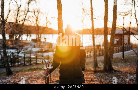 woman walking through a snowy forest with skis at sunset Stock Photo