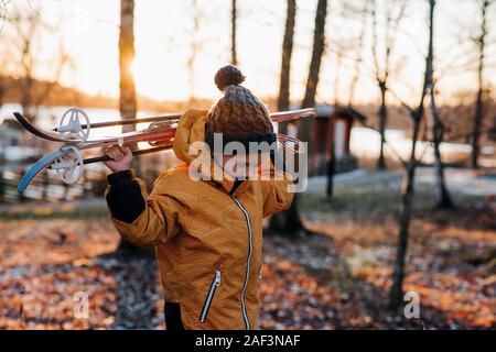 young boy walking through the forest with ski's on his shoulders Stock Photo