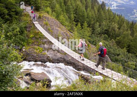 Walkers on the Tour Du Mont Blanc cross a suspension bridge across the meltwater river from the Bionnassay glacier; Stock Photo