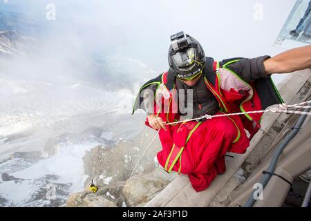 Base jumpers wearing wing suites prepare to jump from the Aiguille Du midi above Chamonix, France, with tourists in a glass cage over the chasm in the Stock Photo