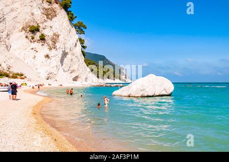 Spiaggia del Frate, Numana, Ancona, Marche, Italy - September 11, 2019: People resting on amazing white pebbles beach surrounded by high massive white Stock Photo