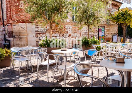 Numana, Ancona, Marche, Italy - September 11, 2019: Young olive trees growing in a big flowerpots with blooming flowers on medieval street of Numana. Stock Photo