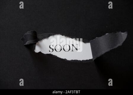 Word SOON printed on a white background with black torn paper. Stock Photo