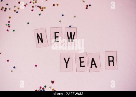 Pink background with sequins of small multi-colored stars and New Year's eve inscription. Flay lay Stock Photo