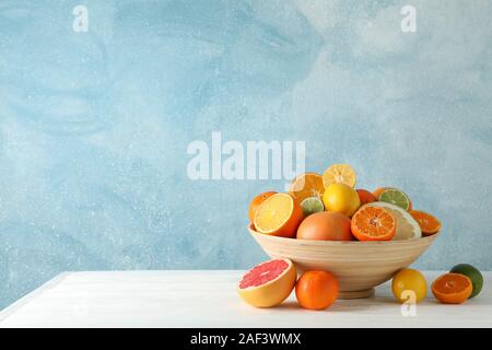 Juicy citrus fruits in bowl on wooden table against blue background, space for text Stock Photo