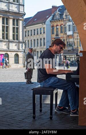 Pedestrian / amateur pianist playing music on public street piano under Gentse Stadshal / Ghent Market Hall in the city Gent, East Flanders, Belgium Stock Photo