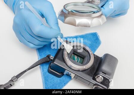 Cleaning the digital camera matrix. Digital camera service. The master in gloves under a magnifying glass cleans the matrix of a digital camera Stock Photo