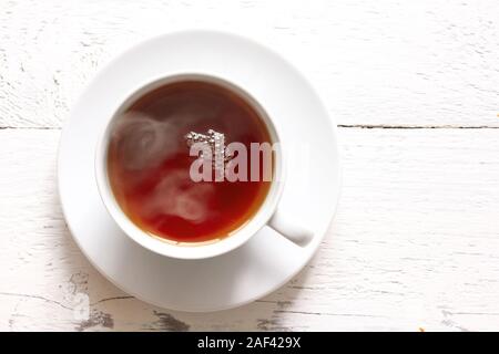 Cup of hot black tea isolated on white painted rustic wood. White porcelain. Top view.