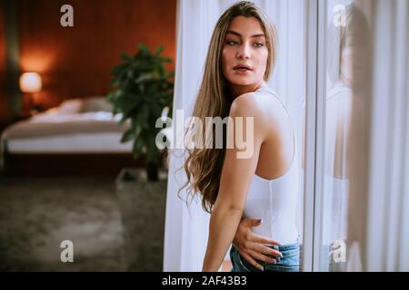 Pretty young woman standing by the window in the room Stock Photo