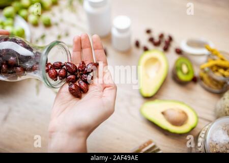 Holding dried rose hips at the table with healthy vegan food ingredients and supplements, top view. Concept of rose hips as a new trend in food and cosmetic industry Stock Photo
