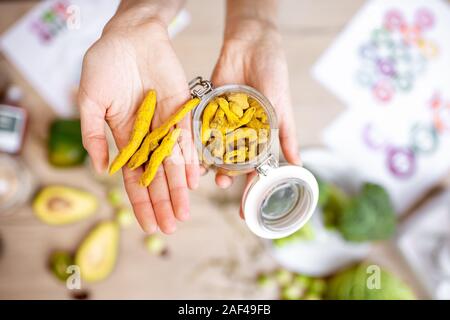 Holding turmeric root at the table with healthy vegan food ingredients and supplements, top view. Concept of curcuma as a new trend in food and cosmetic industry Stock Photo