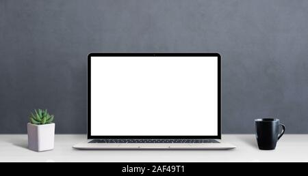 Modern laptop computer on work desk with isolated screen for mockup, app or web site promotion. Clean desk with cup of coffee and plant Stock Photo