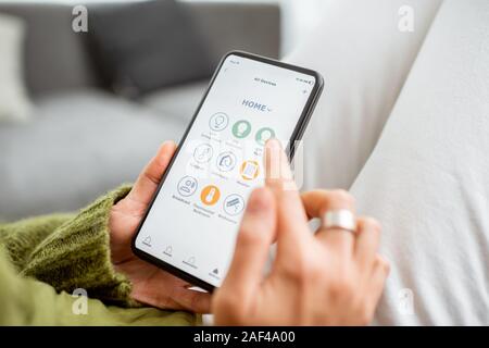 Young woman controlling home with a smartphone. Concept of a smart home and mobile application for managing smart devices at home Stock Photo