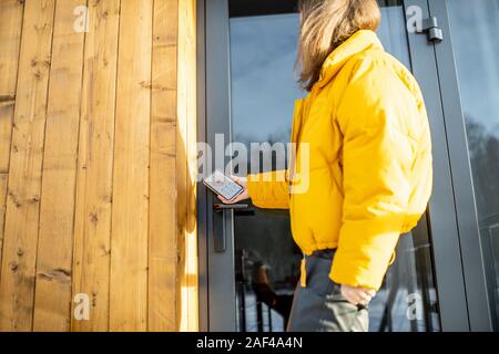 Woman locking smartlock on the entrance door using a smart phone. Concept of using smart electronic locks with keyless access Stock Photo