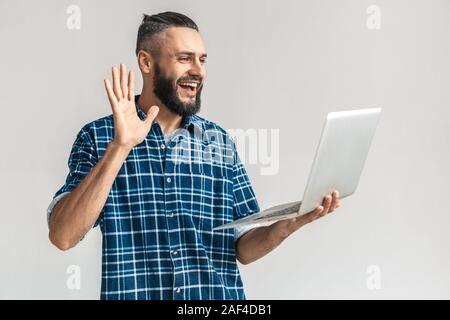 Adult bearded man waving hello, holding laptop in hand Stock Photo