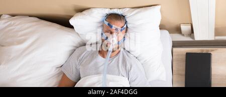 Man Lying On Bed With Sleeping Apnea And CPAP Machine Stock Photo