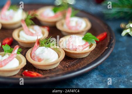 Tartlets with cream cheese and shrimp. Decorated with sprigs of dill and parsley. Seafood. Holiday dish. On a dark background. Copy space. Stock Photo