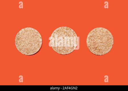 three rice or corn biscuits on an orange-carrot color background, top view of crispy cookies for food design and healthy eating, copy space Stock Photo